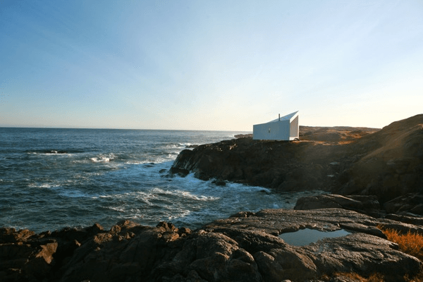 a small white building sitting on top of a rocky shore